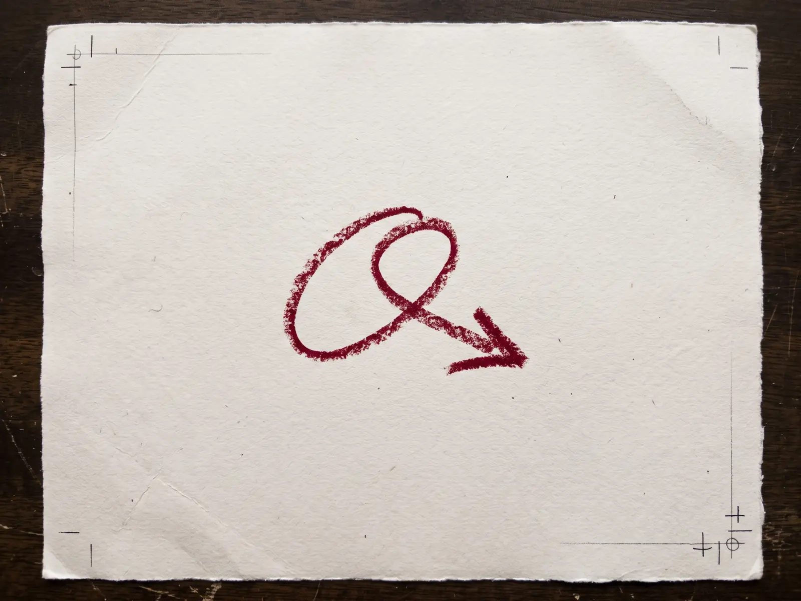 Deep red grease-pencil arrow on warm paper with print registration marks
